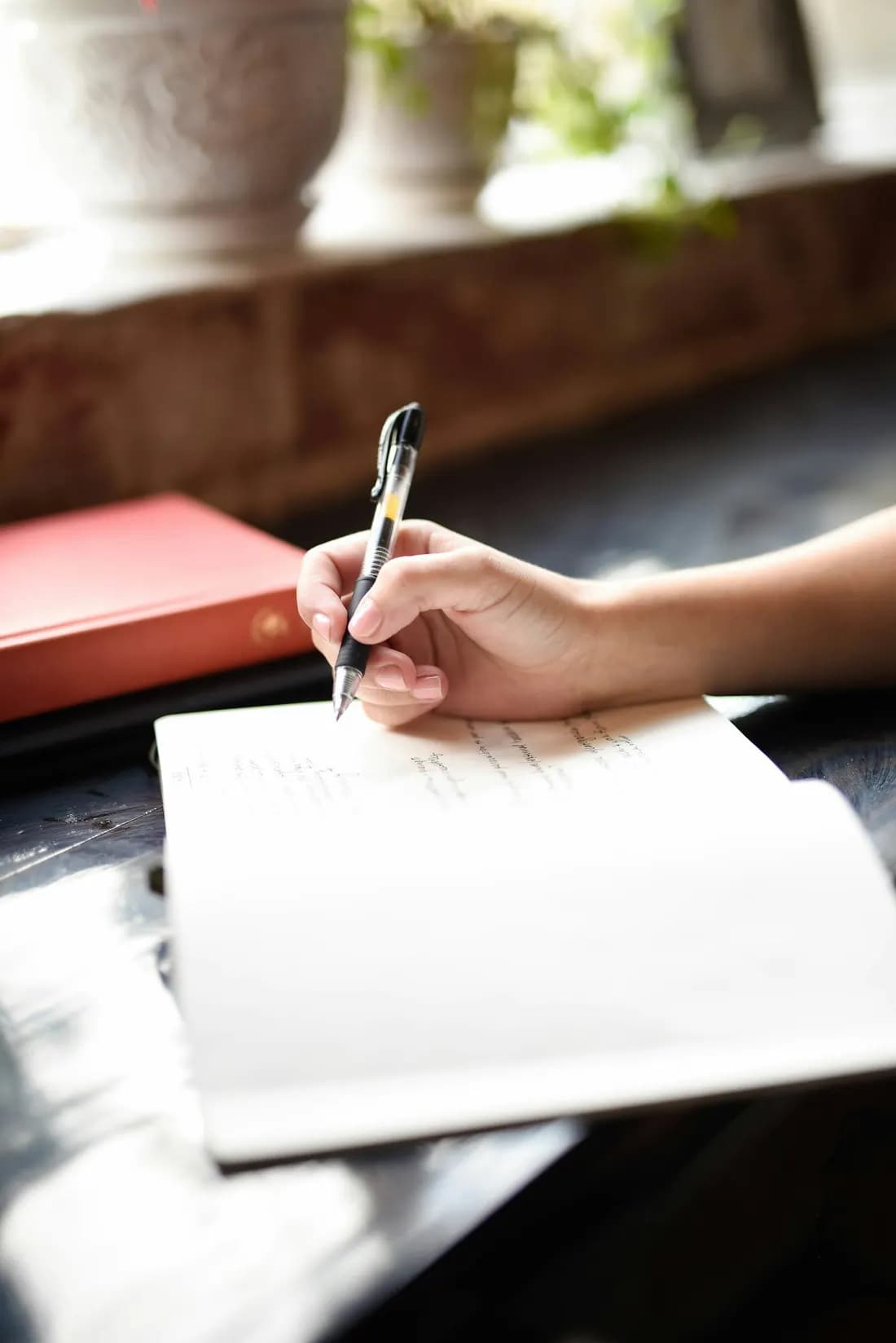 Una mano escribe en un cuaderno junto a la ventana